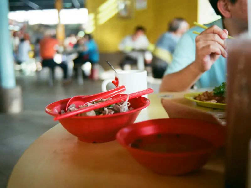 Red bowls on a round table at a hawker centre, with diners eating in the background